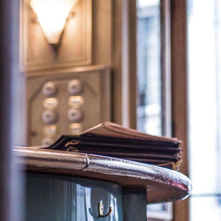 Cartes du menu empilées sur un pupitre près de l'entrée, sous une applique ancienne