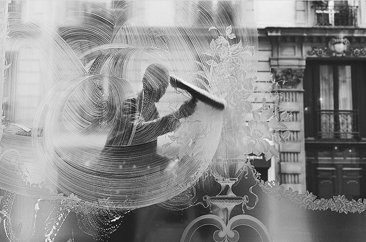 En noir et blanc, nettoyage de la vitrine gravée du café face aux immeubles parisiens