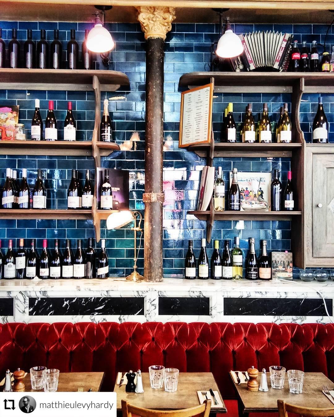 Mur en carrelage bleu, étagères de bouteilles de vin et banquette en velours rouge