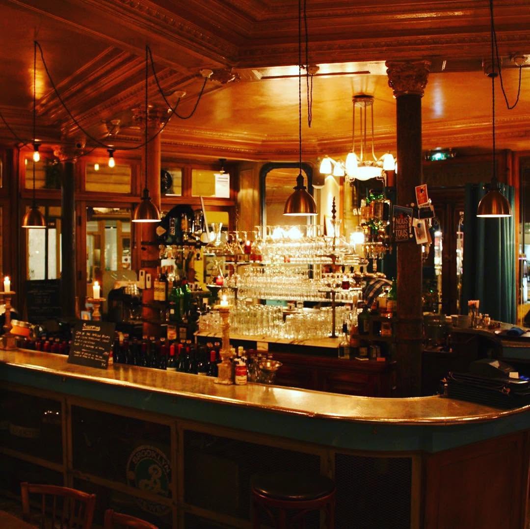 Le comptoir en zinc en angle et ses suspensions dans la lumière chaude du soir