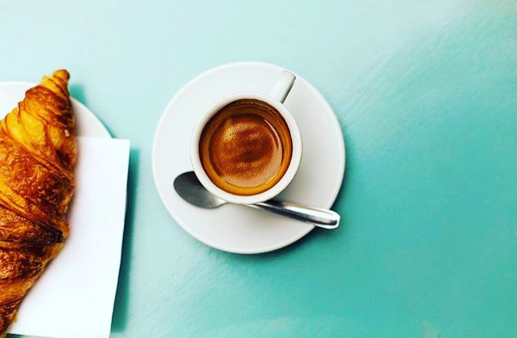 Un espresso et un croissant posés sur une table turquoise, vus de dessus
