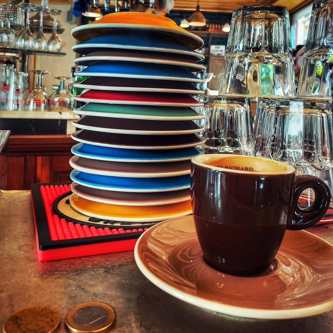 Pile de soucoupes colorées et une tasse d'espresso sur le comptoir en zinc