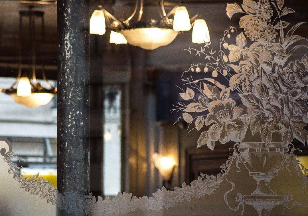 Miroir gravé de motifs floraux reflétant les lustres et la salle du café