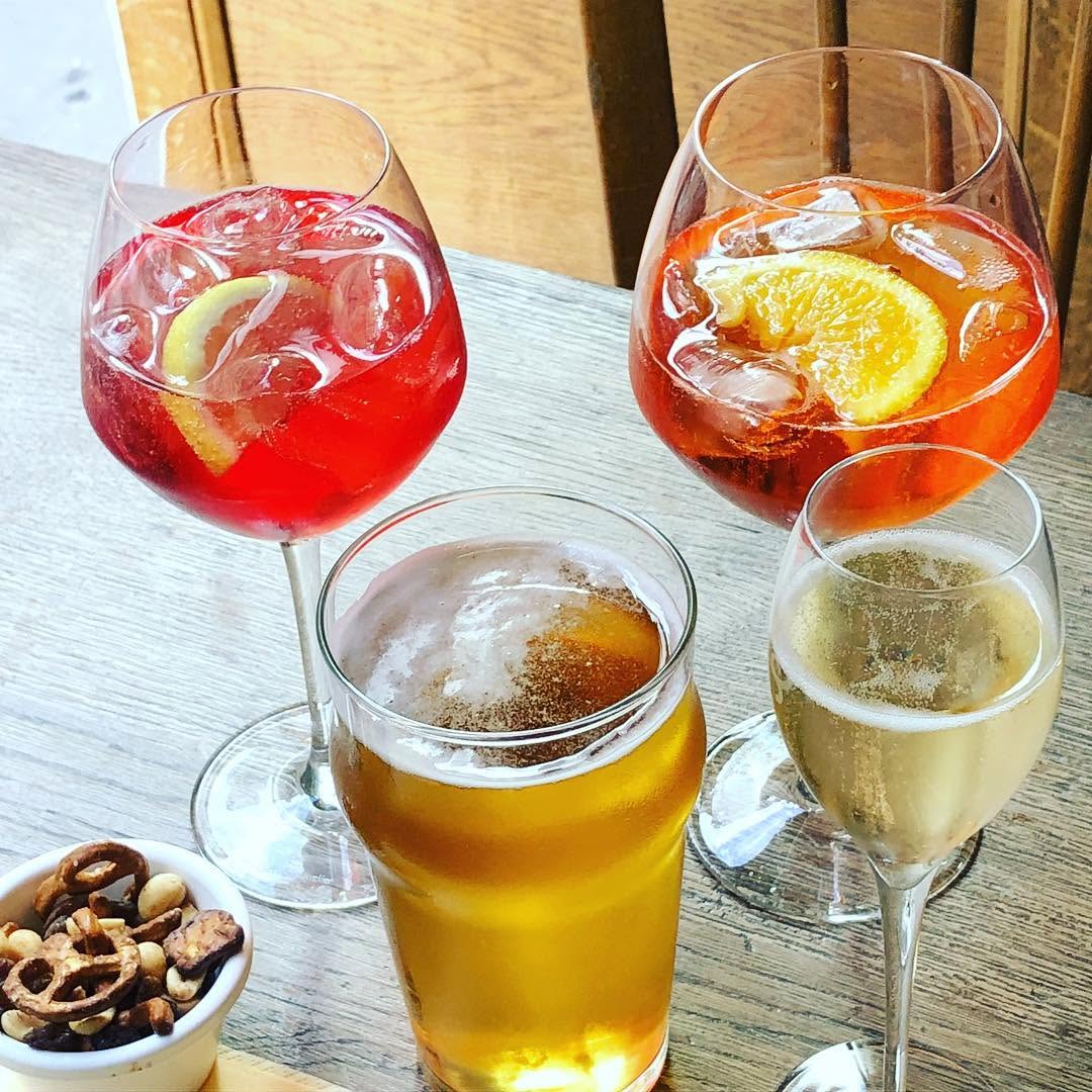 Assortiment d'apéritifs, spritz, bière et champagne, servis avec un bol de fruits secs